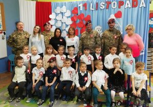 Dzieci z grupy trzeciej wraz nauczycielami, przedstawicielem z biblioteki i żołnierzami pozują do zdjęcia grupowego.