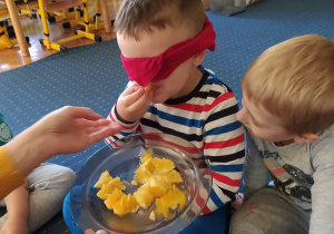 Dziecko z zawiazanymi oczami zgaduje jaki owoc czy warzywo smakuje.