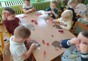 Dzieci naklejają kolce z bibuły na papierowy kształt jeża.