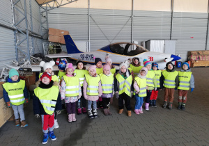 Dzieci z grupy czwartej stoją przed małym samolotem.