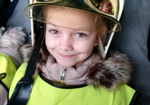 Dziewczynka w kasku strażaka uśmiecha się do zdjęcia.