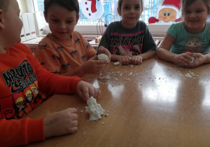 Dzieci siedzą przy stoliku i lepią ze sztucznego śniegu.