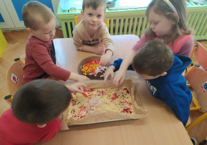 Dzieci nakładają składniki na ciasto.