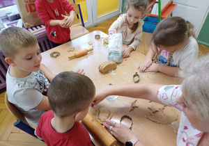 Dzieci siedzące przy stole robią ciastaka cynanonowe.