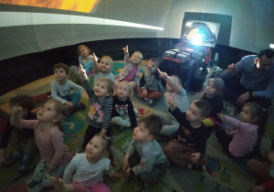 Dzieci oglądają pokaz multimedialny, wskazują planetę Ziemię.