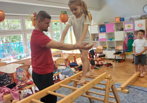 Dziewczynka idąca samodzielnie po drabinkach w asekuracji nauczyciela.