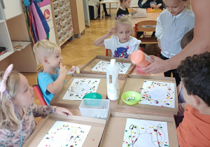 Dzieci obserwują nakładanie farby na swoje prace.