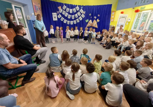 Dyrektor przemawiająca na tle dekoracji oraz ustawionej grupy nr 1 gotowej do występu.