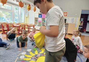 Jubilat wrzucający koraliki do miseczek, w tle cłopiec ogladający zdjęcia położone na słoneczku.