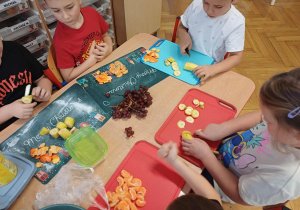 Dzieci siedzące z jubilatem przy pracy podczas robienia szaszłyków.