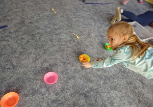 Dziewczynka przekładająca piłeczki z miseczki do miseczki, będąc podparta tylko na rękach - ćwiczenia obręczy barkowej.