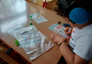 Chłopiec kreśloący liczby na kartach suchościeralnych z wykorzystaniem klepsydry.