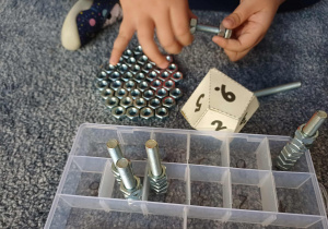 Dziecko nakręca na śrubę nakrętki w ilości wyrzuconej na kostce - ćwiczenie motoryki małej