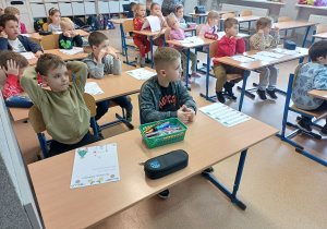 Dzieci siedzące w kalsie szkolnej przy ławkach.