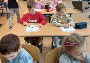 Dzieci pracujące na kartach pracy w ławkach szkolnych.
