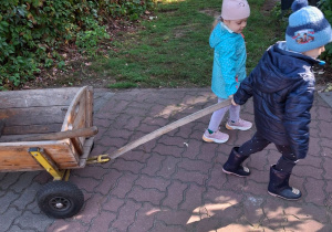 Dziewczynka i chłopiec ciągną wózek.