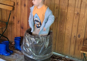 Chłopiec depcze kapustę w drewniane beczce.