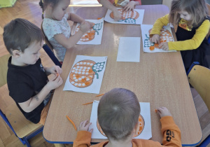 Wyklejanie plasteliną kropek na obrazku przedstawiającym dynię.