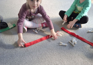 Dzieci przypinają klamerki na szarfę.