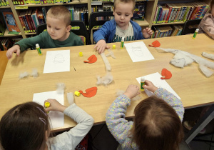 Dzieci przyklejające na kartkę elementy plastyczne.