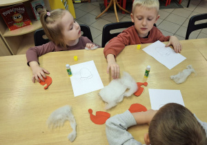 Dzieci przyklejające na kartkę elementy plastyczne.
