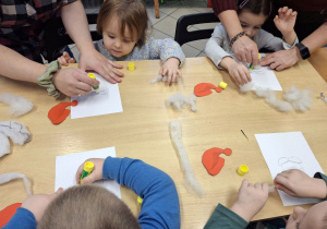 Dzieci przyklejające na kartkę elementy plastyczne.