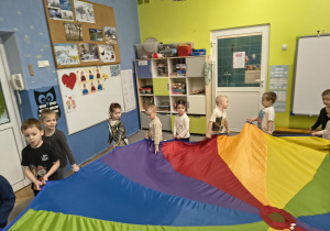 Dzieci śpiewają piosenkę, trzymają chustę animacyjną i chodzą dookoła.