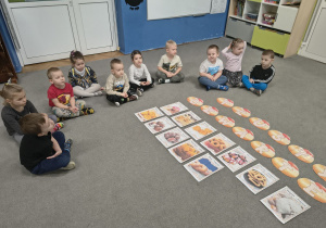 Dzieci siedzą na dywanie i słuchają informacji o tradycjach Tłustego Czwartku.