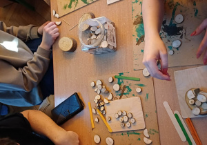 Zdjęcie przedstawiające rodziców z dziećmi wykonujących obrazy na drewnianych deseczkach.