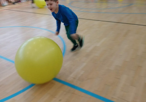 Dziecko biegnące za dużą piłką.