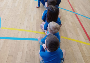 Dzieci siedzące na podłodze jedno za drugim czekając na rozpoczęcie konkurencji