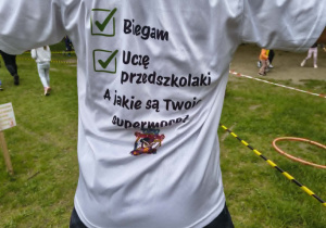 Nauczyciel prezentujący koszulkę z napisem "Biegam, uczę przedszkolaki, a jaka jest twoja supermoc".
