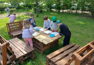 Dzieci wpisują na listę znalezione obiekty na ławie ogrodowej.