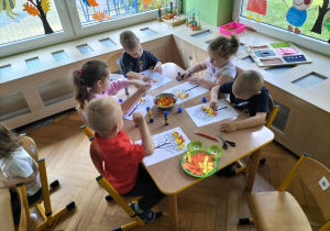 dzieci przyklejają jesienne liście do sylwety drzewa