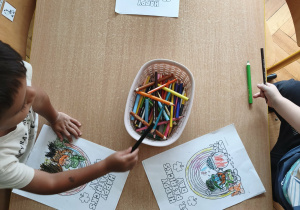 dzieci siedzą przy stoliku i kolorują ilustracje