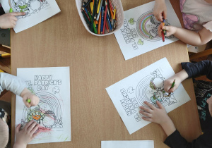 dzieci siedzą przy stoliku i kolorują ilustracje