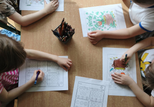 dzieci siedzą przy stoliku i kolorują ilustracje