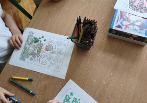 dzieci siedzą przy stoliku i kolorują ilustracje