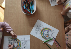 dzieci siedzą przy stoliku i kolorują ilustracje